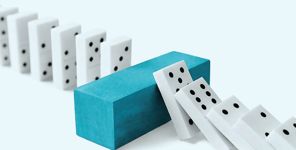 Domino pieces falling toward a blue block barrier symbolizing risk prevention stopping financial loss or cascading failures.