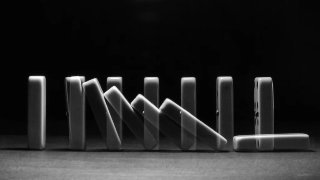 Domino pieces falling in sequence, illustrating a cascading effect or chain reaction of failures.